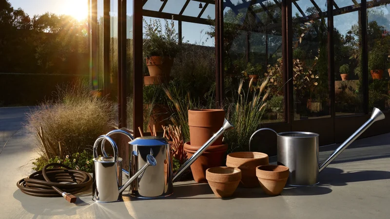 Illustrative watering cans, clay pots and a coiled hose beside a glasshouse door